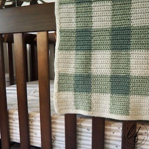 This image shows the sample of this gingham crochet baby blanket pattern draped over the side of a wooden crib.
