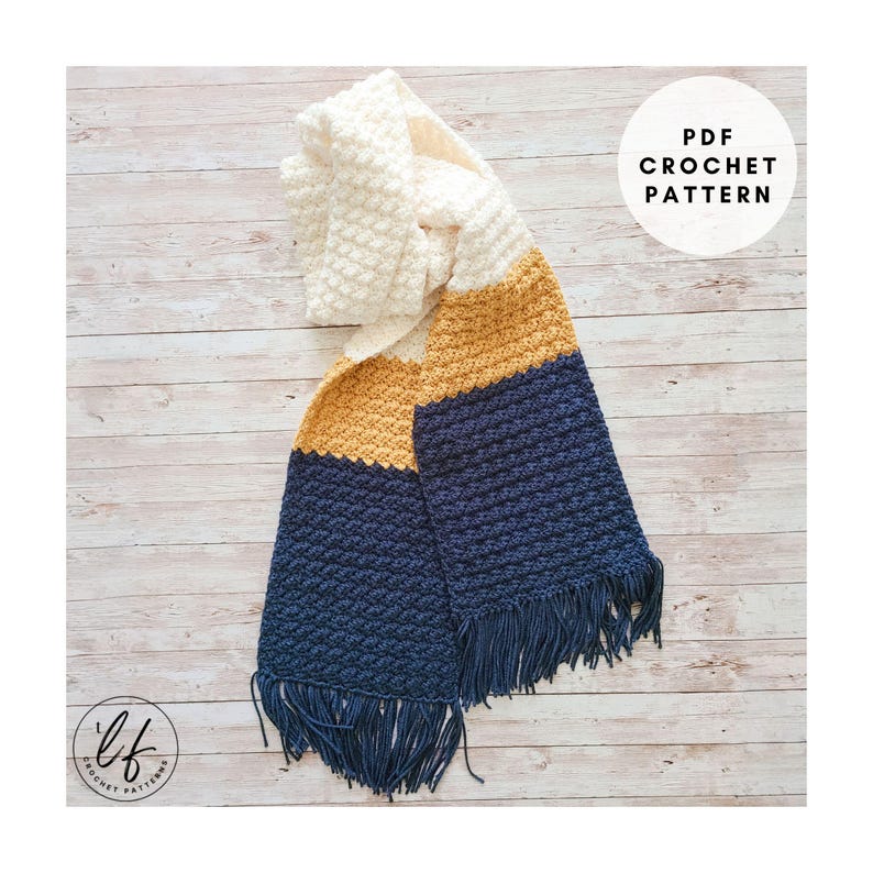 This image shows a sample made from this crochet scarf pattern. The scarf is made in blue, yellow and white and laid flat on a faux wood background.