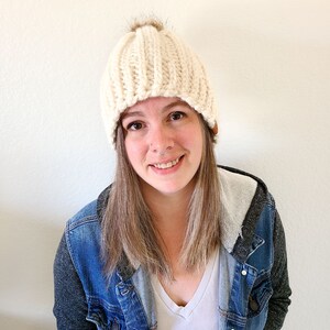 Peut inclure: Bonnet en tricot cr&egrave;me avec un design c&ocirc;tel&eacute; et un pompon en fausse fourrure marron sur le dessus. Le chapeau a une petite &eacute;tiquette en cuir marron sur le c&ocirc;t&eacute;. Cet accessoire est un bonnet d'hiver.