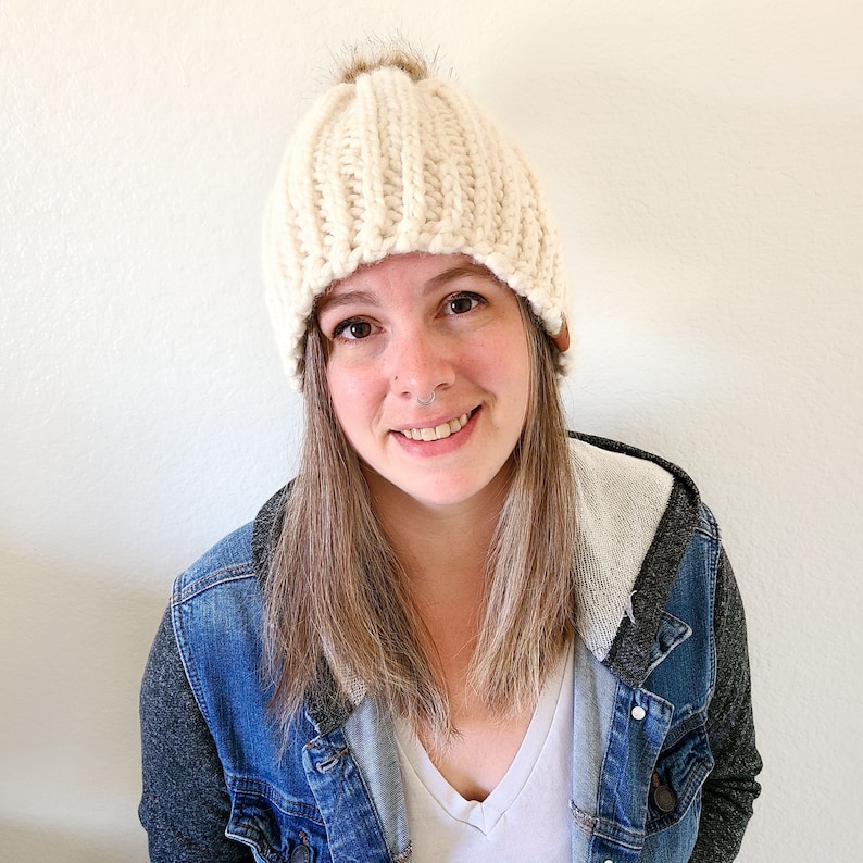 Peut inclure: Bonnet en tricot cr&egrave;me avec un design c&ocirc;tel&eacute; et un pompon en fausse fourrure marron sur le dessus. Le chapeau a une petite &eacute;tiquette en cuir marron sur le c&ocirc;t&eacute;. Cet accessoire est un bonnet d'hiver.