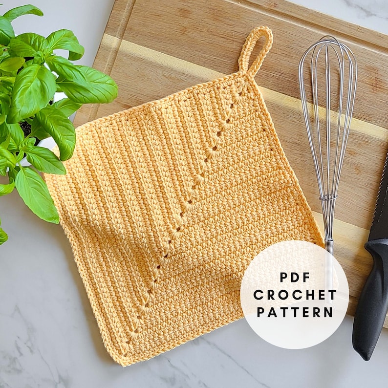 May include: A square, light orange crochet potholder with a loop for hanging. The potholder features a decorative stitch pattern and the text "PDF CROCHET PATTERN" in a white circle. A whisk and knife are visible.