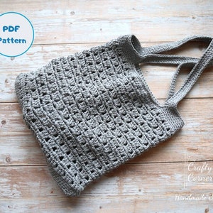 K&ouml;nnte beinhalten: Eine graue geh&auml;kelte Einkaufstasche mit breiten Henkeln. Die Tasche ist mit einem einfachen Stichmuster gearbeitet und hat einen l&auml;ssigen, ungezwungenen Look. Das Bild enth&auml;lt den Text "PDF Pattern" und "The Crafty Corner Handmade By Mei".