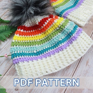 May include: A rainbow striped crochet hat with a white brim and a fluffy black pom pom. The hat is lying on a light wood surface. The text "PDF PATTERN" is printed below the hat.