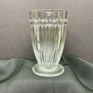 May include: A clear glass drinking glass with a star-shaped design around the rim and vertical lines down the sides. The glass has a wide base.
