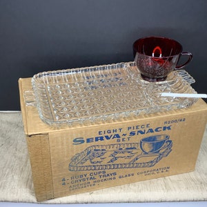 May include: A vintage glass snack set in its original box. The set includes four ruby red cups, four crystal trays, and a serving tray. The box is brown with blue text that reads "Eight Piece Serva Snack Set R200/42 4-Ruby Cups 4-Crystal Trays Anchor Hocking Glass Corporation Lancaster, Ohio, U.S.A."