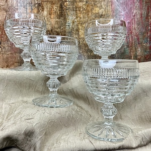 May include: Four clear glass goblets with a textured, diamond-like pattern. The goblets have a wide bowl and a tall, slender stem.