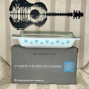 May include: A vintage Pyrex 1 1/4 quart Space Saver Casserole dish with a blue snowflake design. The dish is in its original box, which is gray with a snowflake design.