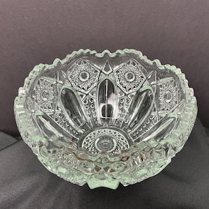 May include: A clear glass bowl with a scalloped edge and intricate cut-glass design. The bowl has a starburst pattern and a raised center.