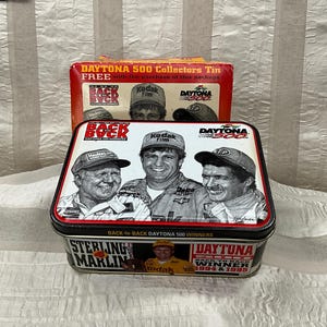 May include: A rectangular tin featuring images of race car drivers and the text "DAYTONA 500 Collectors Tin". The tin has a black border and a red and white lid. The text "BACK-to-BACK DAYTONA 500 WINNERS" is also visible.