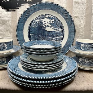 May include: A complete blue and white dinnerware set featuring a landscape design. The set includes plates, bowls, saucers, and teacups. The plates and bowls are stacked, and the teacups are on saucers. The set is arranged on a light-colored surface.