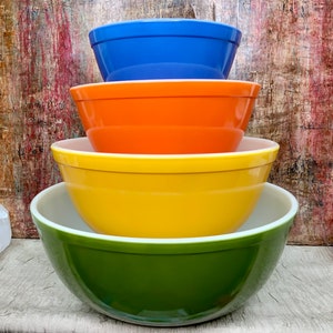 May include: A set of four nesting mixing bowls in green, yellow, orange, and blue. The bowls are made of glass and have a vintage look.