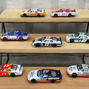 May include: A collection of toy race cars in various colors, including red, yellow, blue, and green, with the number 17 prominently displayed. The cars are arranged on wooden shelves, showcasing their detailed designs and sponsor logos.