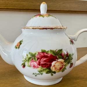 Peut inclure: Théière en porcelaine blanche avec couvercle, ornée d'un motif floral de roses rouges, roses et jaunes. La théière a une bordure dorée et une anse incurvée. Un accessoire de thé classique.