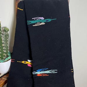Puede incluir: Manta negra tejida con diseños de pájaros coloridos. La manta tiene un borde con flecos y una etiqueta rectangular que dice "Sedona Blanket". Los diseños de pájaros son en tonos de azul, naranja, amarillo, rosa y verde.