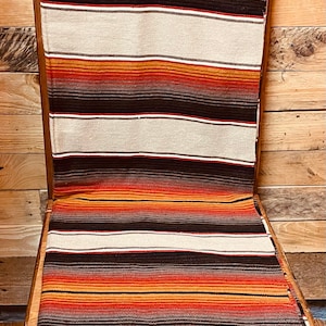 May include: A wooden chair with a striped blanket draped over it. The blanket is brown, orange, and white with a small brass tag that reads "The Original Sedona Blanket Co."