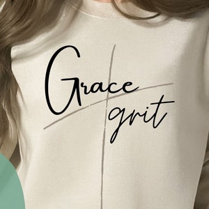 May include: A beige sweatshirt with the text "Grace grit" written in black cursive script over a black cross graphic.