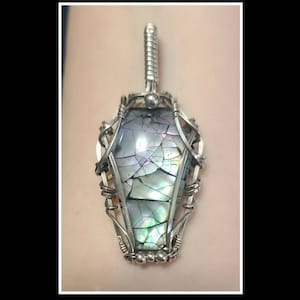 May include: A silver wire-wrapped pendant featuring a large iridescent abalone shell in the shape of a coffin.