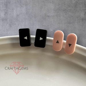 May include: Four small, flat, rectangular buttons with a triangle symbol. Two buttons are black and two are pink.