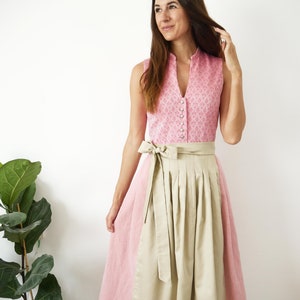 Puede incluir: Un vestido tradicional alem&aacute;n, llamado dirndl, de color rosa y beige con un corpi&ntilde;o blanco con botones y una falda beige. El corpi&ntilde;o tiene un estampado floral.