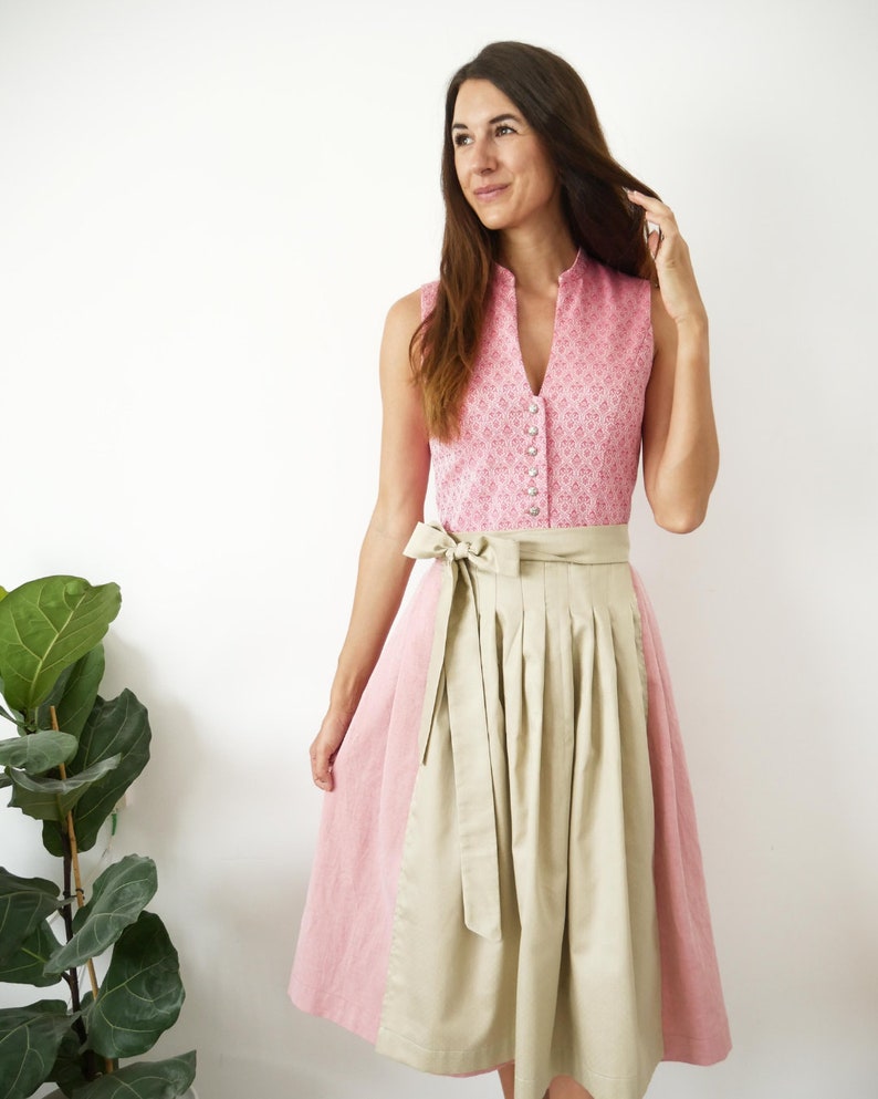 Puede incluir: Un vestido tradicional alem&aacute;n, llamado dirndl, de color rosa y beige con un corpi&ntilde;o blanco con botones y una falda beige. El corpi&ntilde;o tiene un estampado floral.