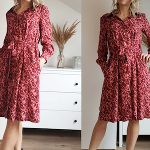 May include: A red and pink patterned long-sleeved dress with a button-up front and a tie belt.
