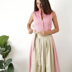 Puede incluir: Un vestido tradicional alem&aacute;n, llamado dirndl, de color rosa y beige con un corpi&ntilde;o blanco con botones y una falda beige. La falda tiene pliegues y un cintur&oacute;n a juego.