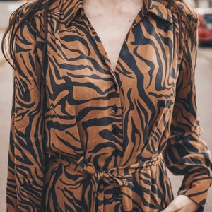 May include: A brown and black long-sleeved dress with a tiger print. The dress has a button-up front and a tie belt at the waist.