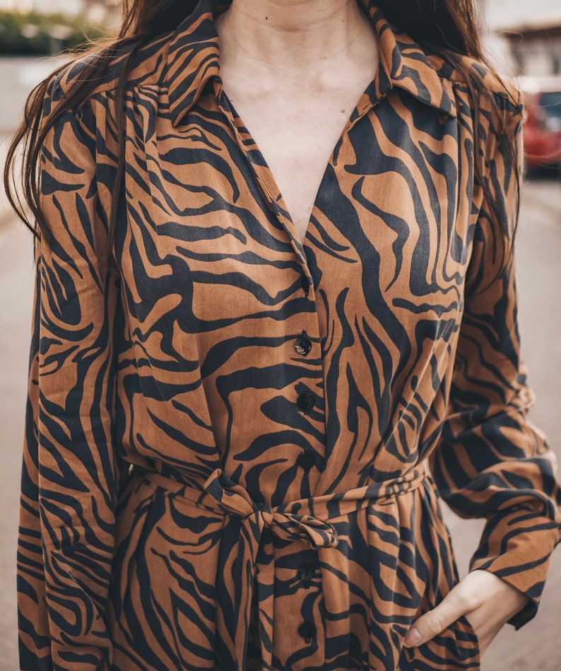 May include: A brown and black long-sleeved dress with a tiger print. The dress has a button-up front and a tie belt at the waist.