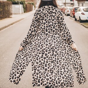 May include: A woman wearing a long, brown and black leopard print dress with a black hat walking down a street.