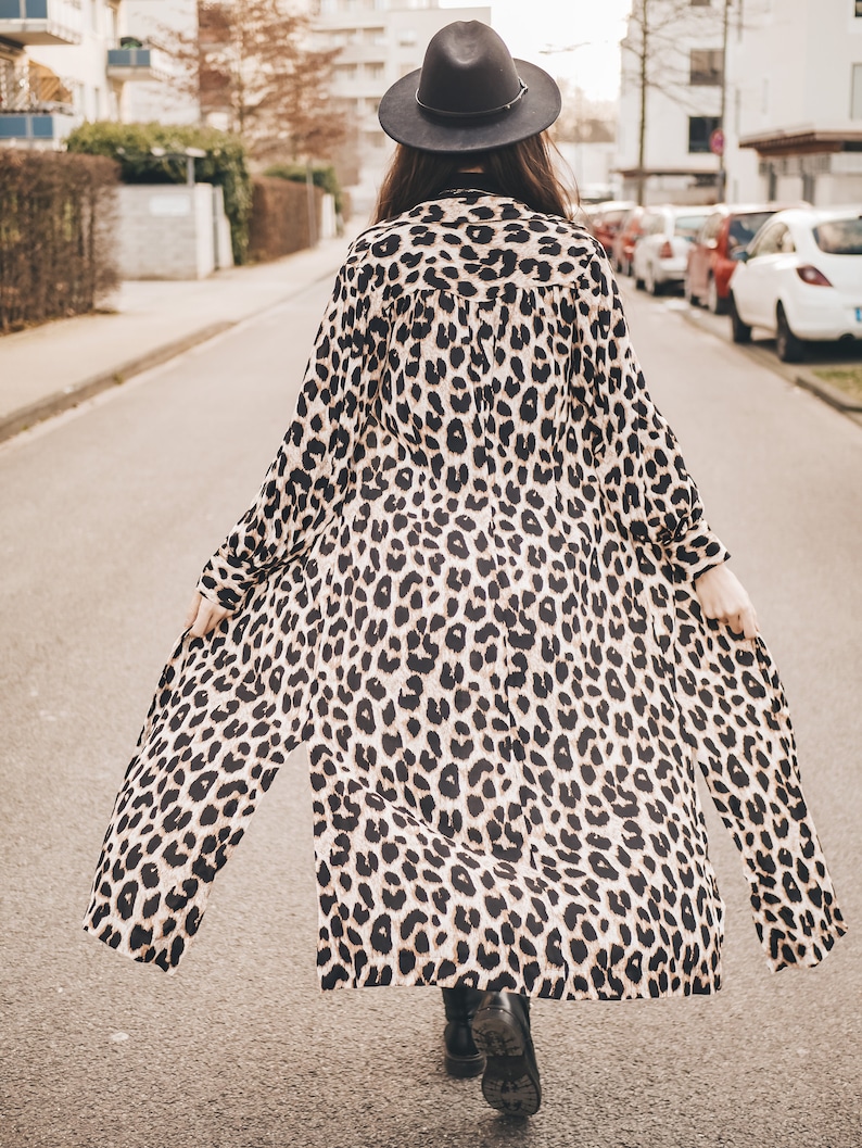 May include: A woman wearing a long, brown and black leopard print dress with a black hat walking down a street.