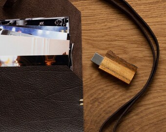 May include: A brown leather envelope with a stack of photos inside. A wooden USB drive with a brown leather strap is on a wooden surface.