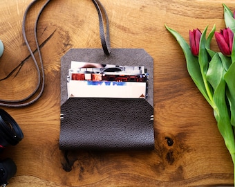May include: A brown leather photo album with a strap. The album is open and filled with photos. The album is on a wooden surface with a potted cactus and a bouquet of red tulips.