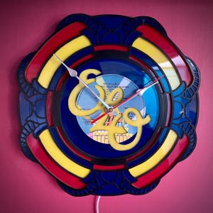 May include: A clock made from a vinyl record with a blue, yellow, and red frame. The record is from the Electric Light Orchestra album "Out of the Blue".