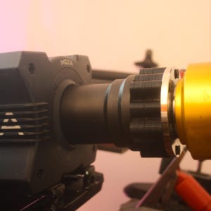 Pode incluir: Close-up de uma base de volante de corrida preta com um adaptador dourado e prateado. A base tem um logotipo MOZA preto e prateado no lado.