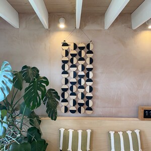 Könnte beinhalten: Ein geometrischer Wandbehang in Schwarz und Weiß aus Holzkreisen. Die Kreise sind in einem sich wiederholenden Muster aus halb schwarz und halb weiß angeordnet. Der Behang ist mit einer Schnur an der Decke befestigt.
