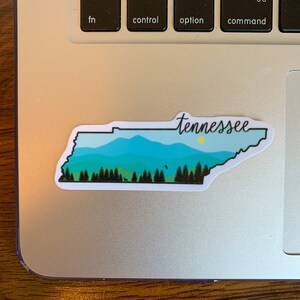 May include: A sticker of the state of Tennessee with a blue and green mountain landscape and the word "Tennessee" written in cursive.