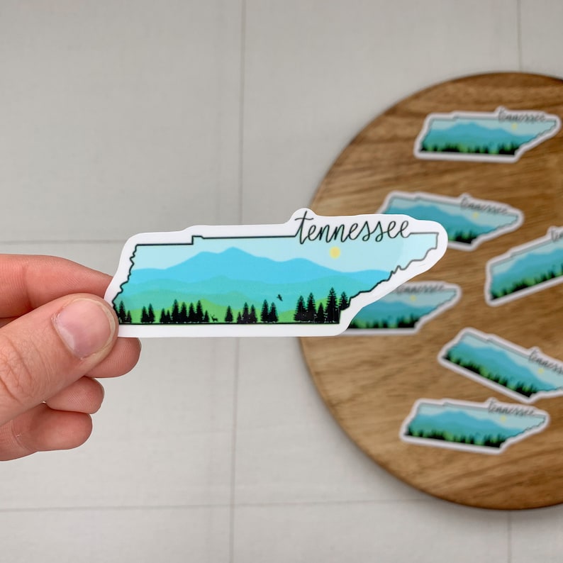 May include: A sticker of the state of Tennessee with a blue and green mountain landscape and the word "Tennessee" written in cursive.