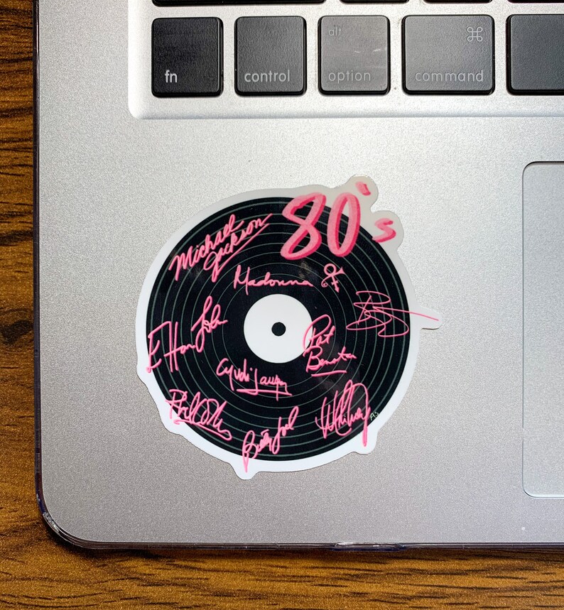 May include: A black vinyl record sticker with the text "80's" in pink lettering. The sticker features the signatures of various 80's music artists, including Michael Jackson, Madonna, and Phil Collins.