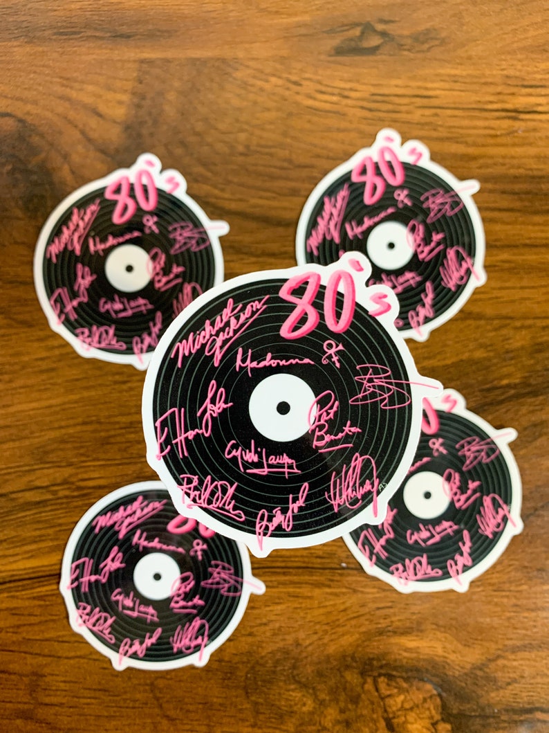 May include: Five black and white vinyl record stickers with pink 80's text. The stickers feature the signatures of popular 80's musicians including Michael Jackson, Madonna, and Billy Joel.