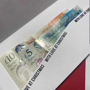 May include: A white envelope with a red border. The envelope is open and contains several British pound notes. The text "WITH LOVE AT CHRISTMAS" is printed on the envelope.