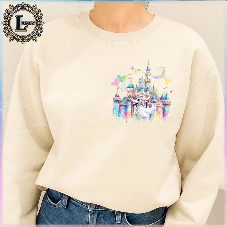Puede incluir: Sudadera de color crema con un dise&ntilde;o de acuarela colorido de un castillo, Zero el perro fantasma y orejas de Mickey Mouse. El dise&ntilde;o utiliza colores pastel y tiene una est&eacute;tica caprichosa. La sudadera tiene cuello redondo y mangas largas.