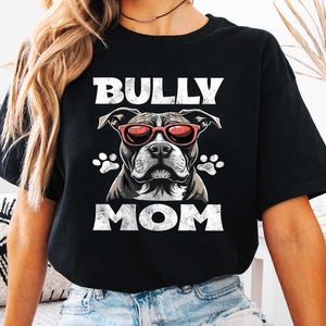 以下が含まれることがあります： 白いグラフィックでピットブルがサングラスをかけて「BULLY MOM」という文字が書かれた黒いTシャツ。