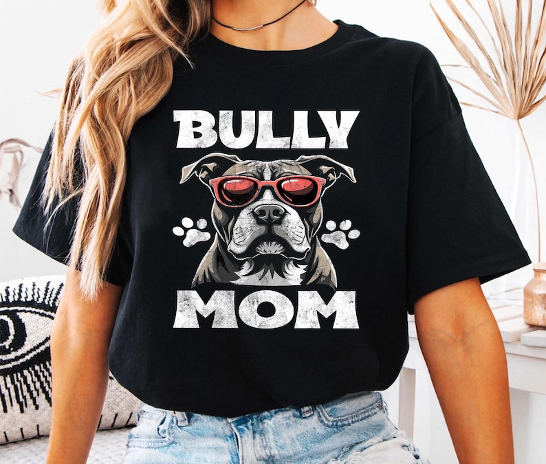 以下が含まれることがあります： 白いグラフィックでピットブルがサングラスをかけて「BULLY MOM」という文字が書かれた黒いTシャツ。
