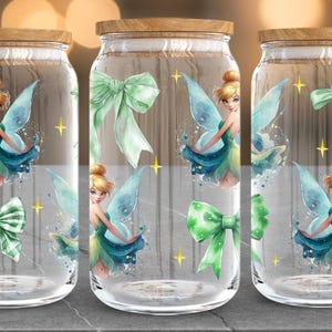 Puede incluir: Tres tarros de vidrio con tapas de madera, cada uno adornado con una ilustraci&oacute;n de hada en tonos azules, verdes y amarillos. Los tarros tambi&eacute;n presentan lazos verdes y acentos de estrellas doradas, creando una est&eacute;tica caprichosa.