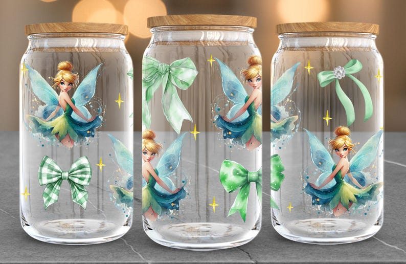Puede incluir: Tres tarros de vidrio con tapas de madera, cada uno adornado con una ilustraci&oacute;n de hada en tonos azules, verdes y amarillos. Los tarros tambi&eacute;n presentan lazos verdes y acentos de estrellas doradas, creando una est&eacute;tica caprichosa.