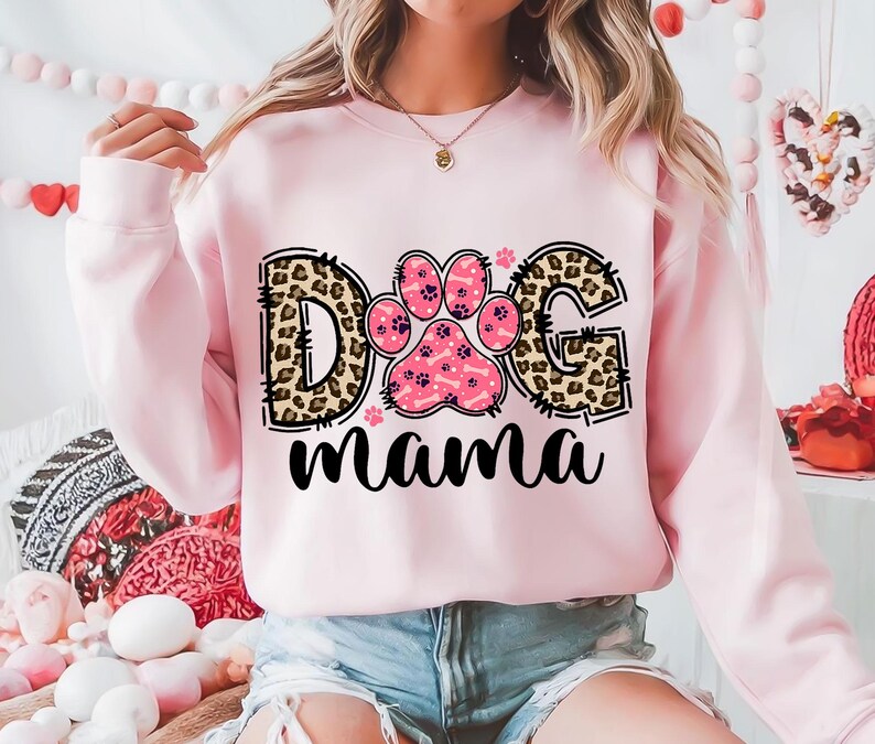 以下が含まれることがあります： 「Dog Mama」と書かれた、レオパード柄と肉球のプリントが施されたピンク色のスウェットシャツです。