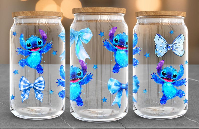 Puede incluir: Tres frascos de vidrio transparente con tapas de madera. Cada frasco presenta un personaje de dibujos animados azul, lazos azules y estrellas azules. El personaje tiene ojos grandes y est&aacute; en una pose juguetona. Los frascos est&aacute;n sobre una superficie gris.