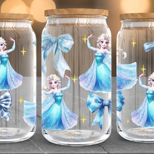 Puede incluir: Tres frascos de vidrio con tapas de madera, decorados con ilustraciones de una princesa con un vestido azul, lazos y estrellas doradas. Los frascos son transparentes y la princesa est&aacute; en una pose de baile.