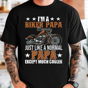 Puede incluir: Camiseta negra con un dise&ntilde;o gr&aacute;fico blanco que presenta una motocicleta y el texto "Soy un pap&aacute; motorista como un pap&aacute; normal, excepto mucho m&aacute;s genial".
