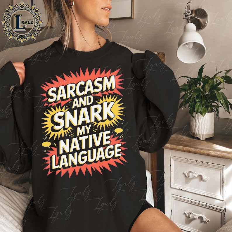 May include: Black sweatshirt with the text "Sarcasm and Snark My Native Language" in a colorful, comic-book style design. The text is in white, yellow, and red, with a burst effect around the words. The sweatshirt is a casual garment.
